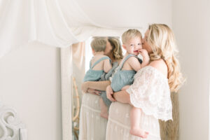 Pregnant mama kissing her oldest baby in front of a mirror. Light and airy maternity style photographed by a Southern California Maternity Photographer
