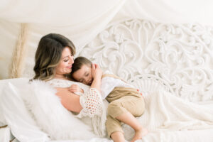 Pregnant mama kissing her oldest child in a natural light studio on a bed. Light and airy maternity style photographed by a Southern California Maternity Photographer