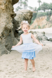 Little girl spins at the beach during a photoshoot holding her dress she purchased at Once upon a Child in Oceanside, California