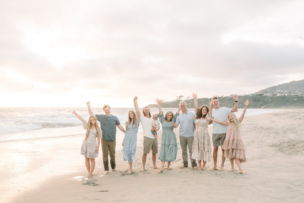 Large family is happy with their hands in the air at a beautiful sunset in Dana Point. Taken by a local photographer who specializes in Beach Family Portraits and Orange County Mini Sessions.