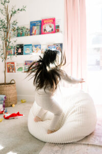 Little girl jumping for joy onto a bean bag in her bedroom located in Orange County, California.