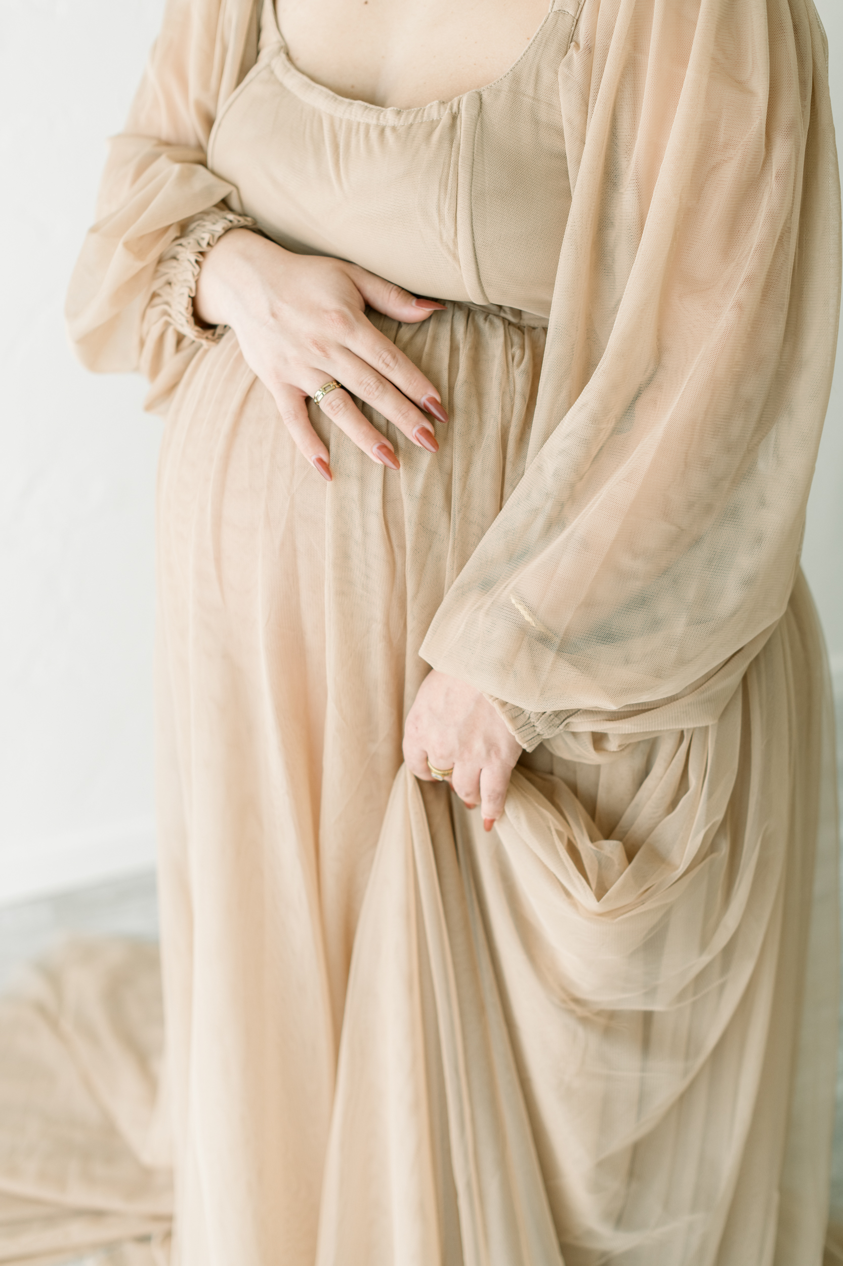 Closeup of a pregnant woman's hand on her bump in a beige maternity gown