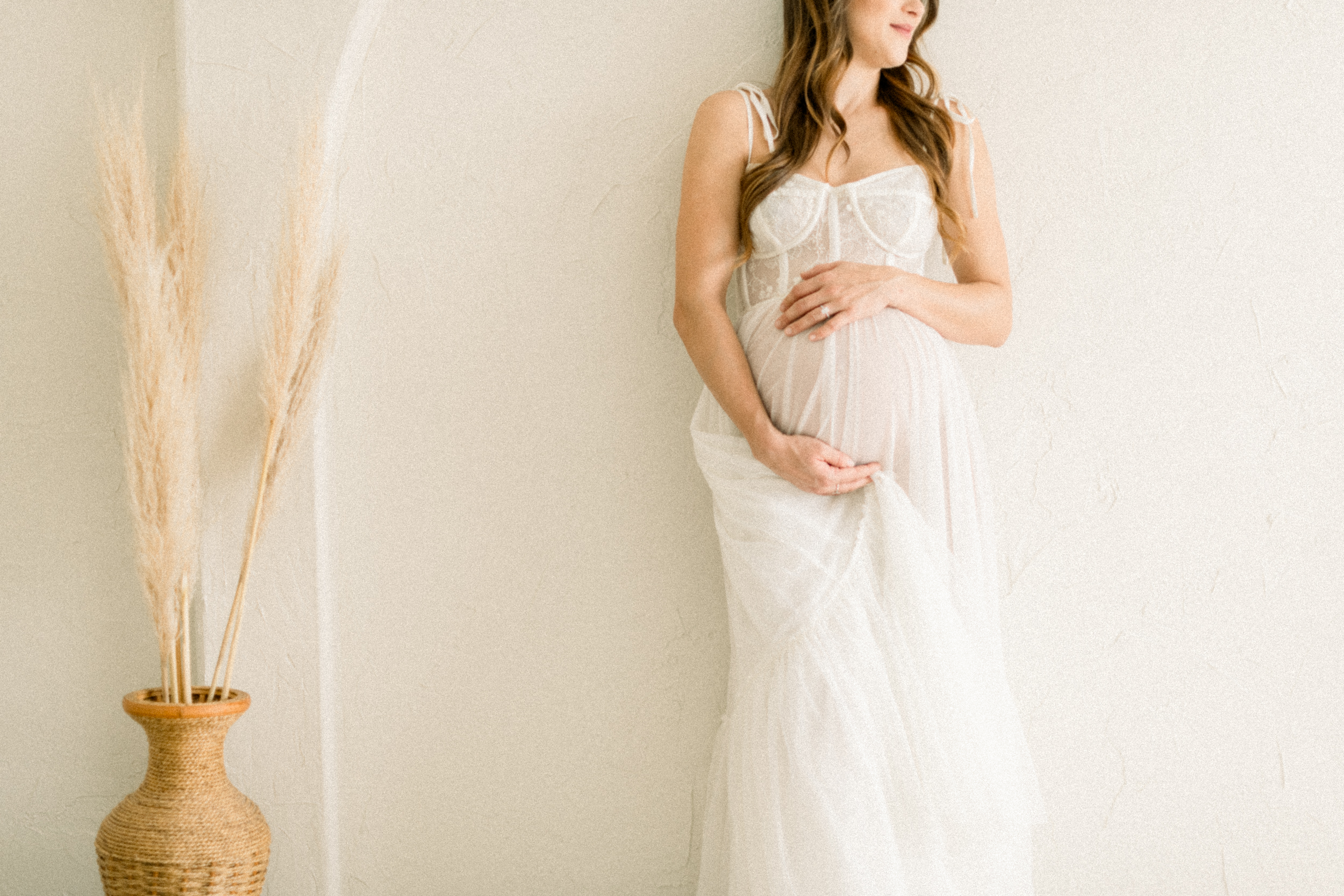 A look at a mother to be leaning on a plaster wall in a studio with hands around her bump after visiting baby shower venues in orange county