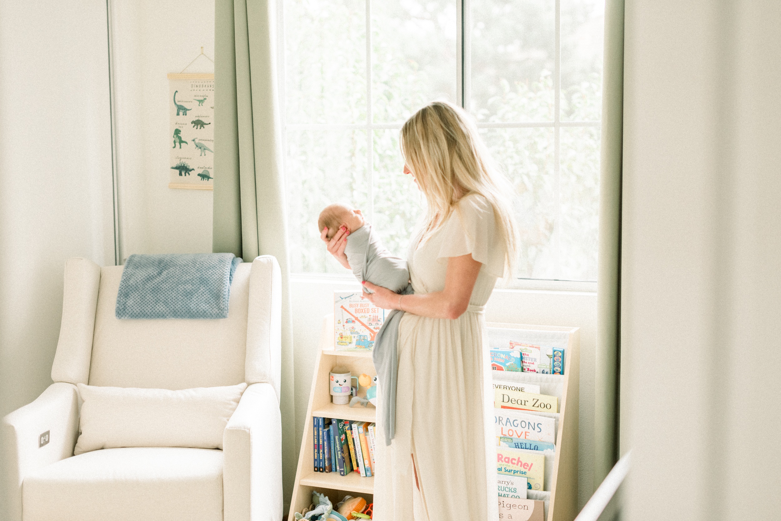 A newborn baby sleeps in mom's hands as she stands in a nursery window