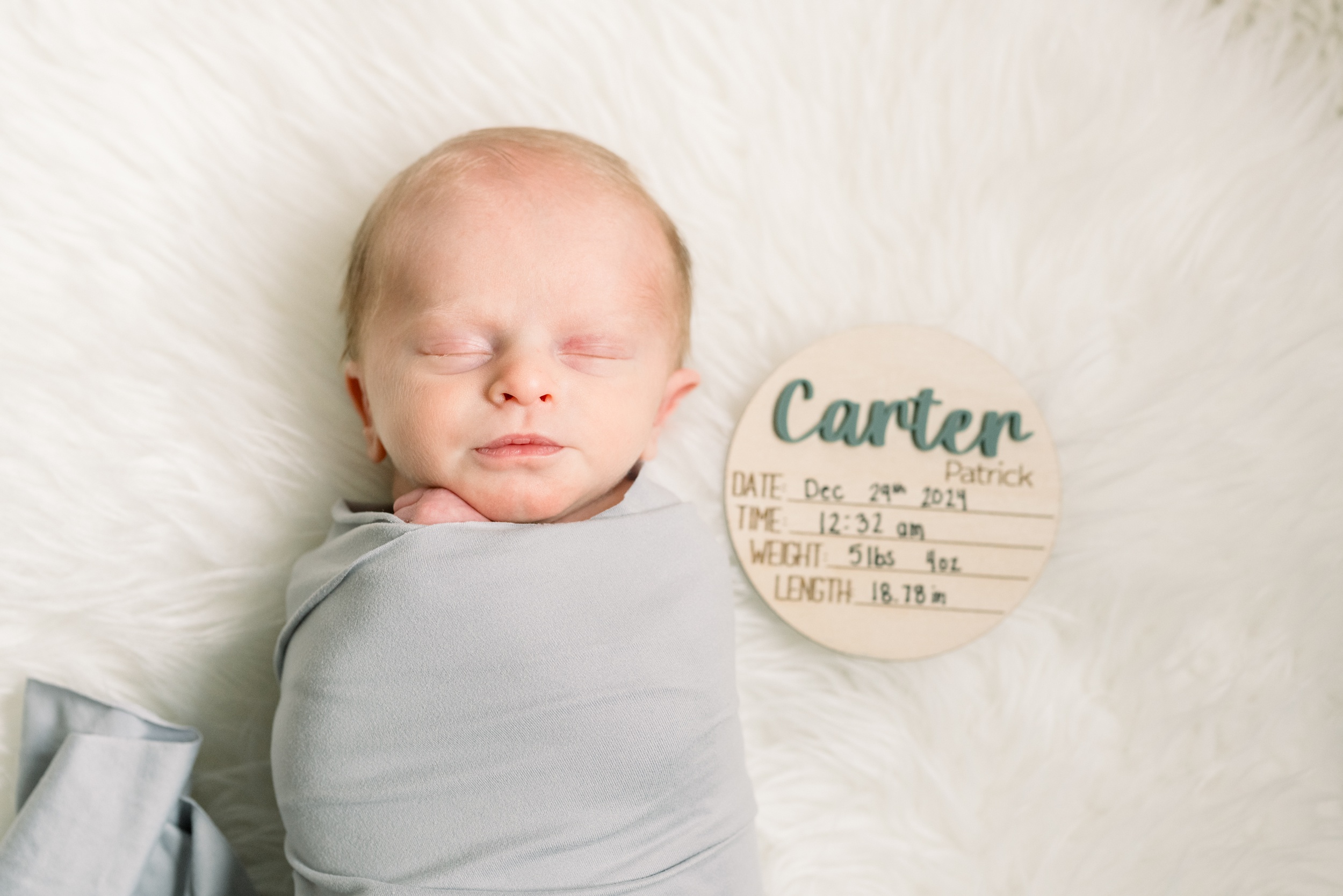 A newborn baby sleeps in a grey swaddle with a name plate with birth details after visiting baby stores in Orange County