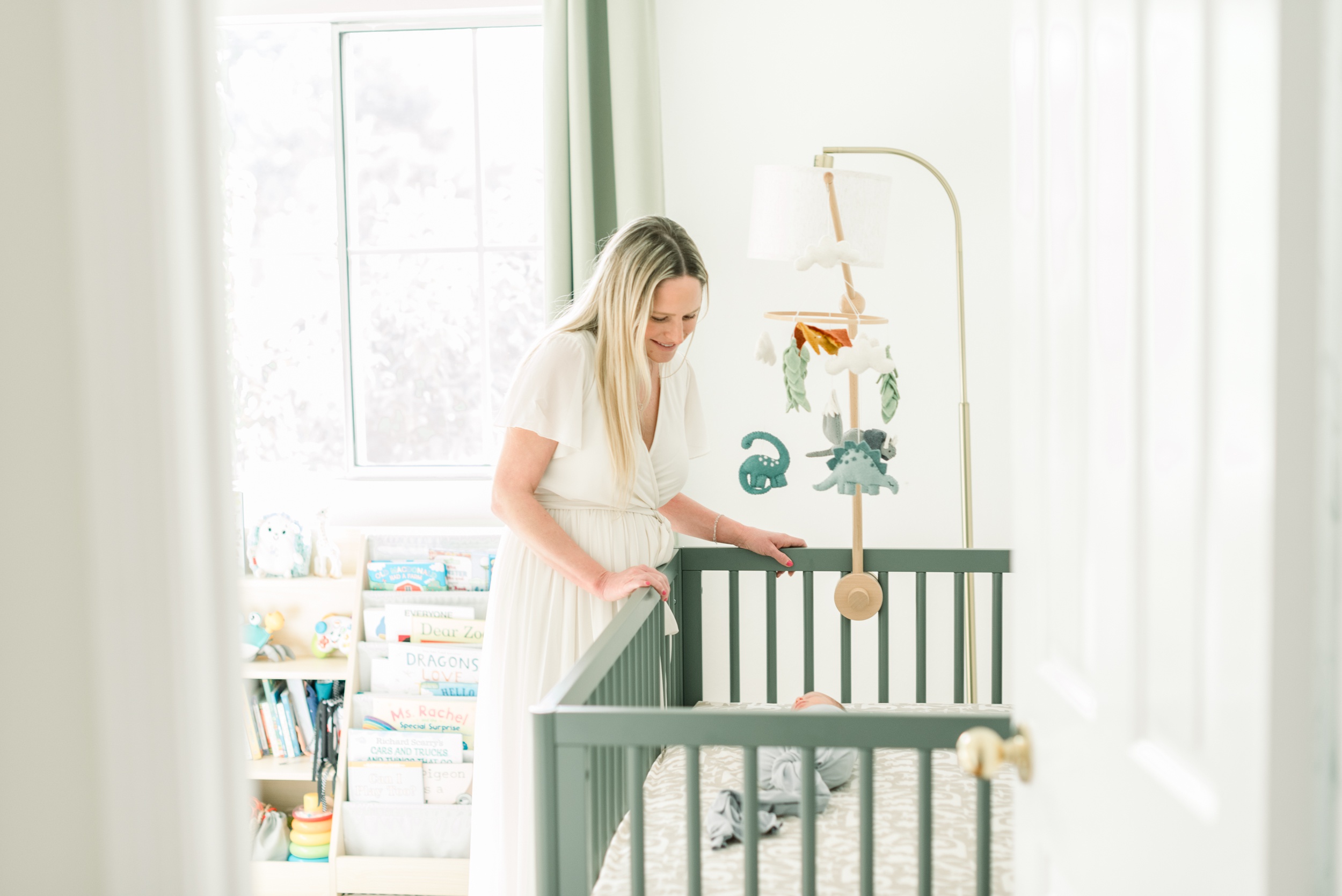 A happy new mom smiles down at her sleeping newborn in a green crib in the nursery after visiting baby stores in orange county