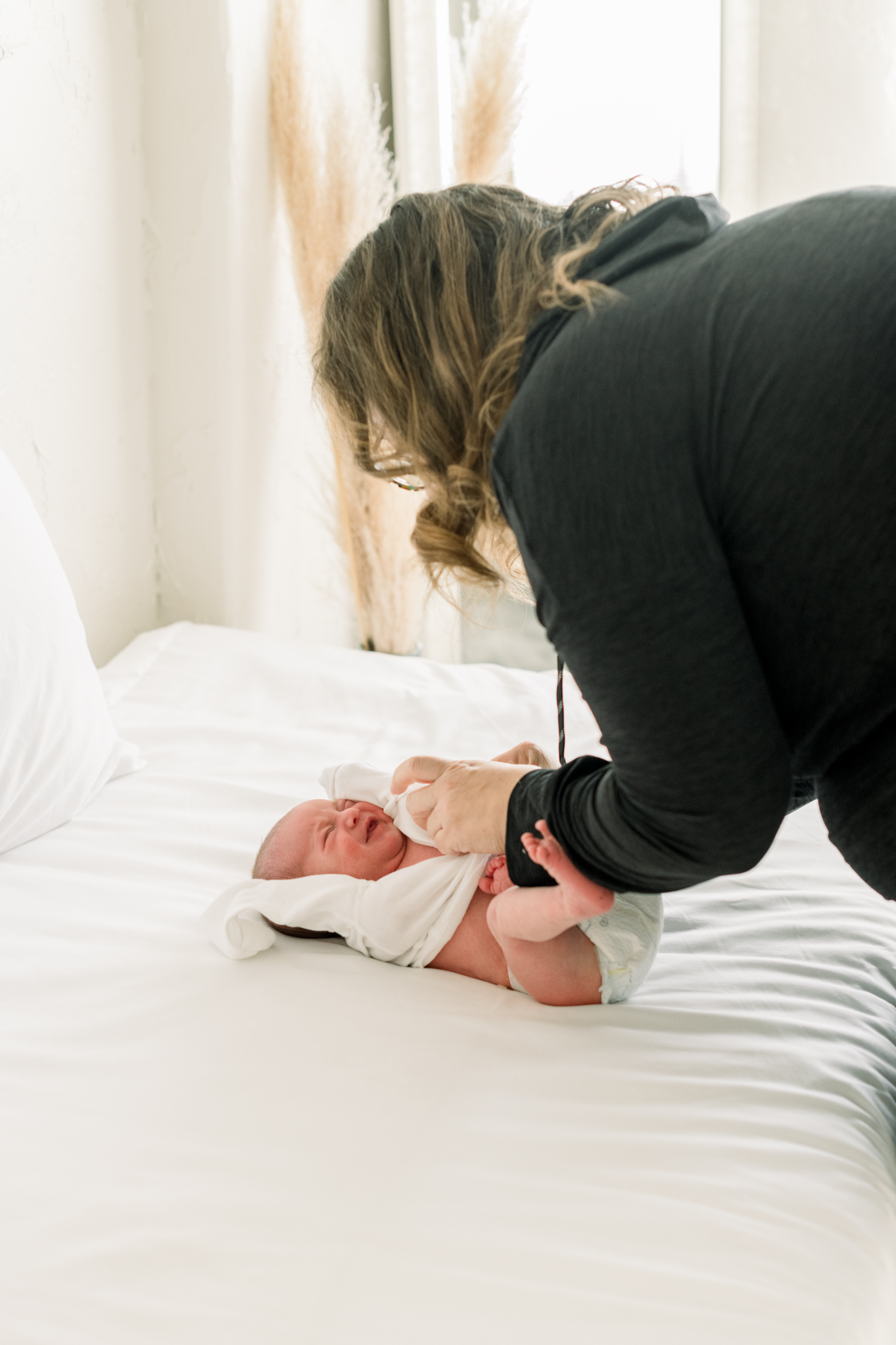 A new mother changes her baby's onesie on a white bed after finding a diaper service in orange county