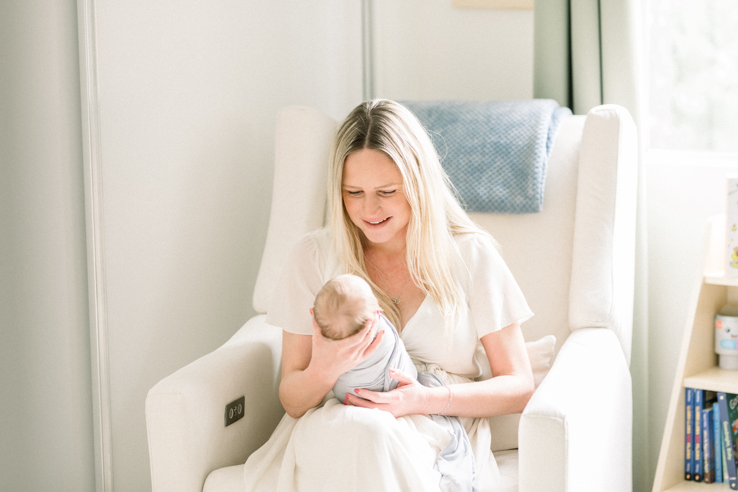 A happy new mom sits in a nursing chair smiling down at her newborn baby in her hands after some pelvic floor therapy in orange county