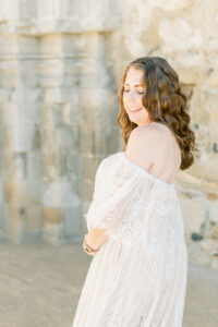 Wind catches beautiful pregnant mamas hair as she poses in a lace dress in Amy Captures Love Client closet at the Mission San Juan Capistrano in Orange County, California.