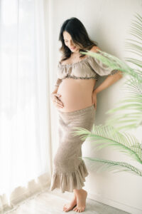 Woman posing for her maternity pictures which give a warm costal california vibe after deciding to use one of Amy Captures Love Client closet pieces for her maternity photoshoot.