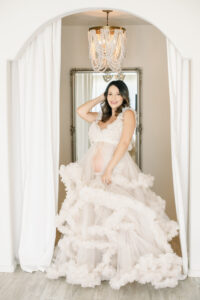 Pregnant mama wearing a flowy, tulle, ruffle gown while posing in the studio located in Huntington Beach, California with Amy Captures Love