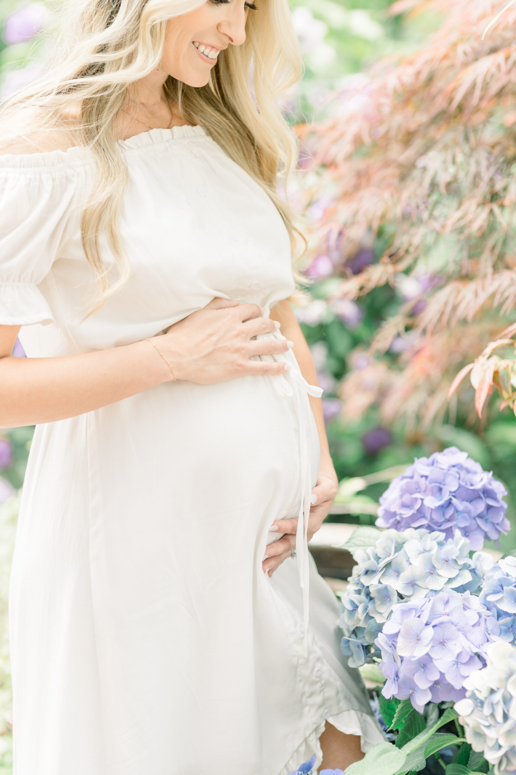 Woman stands in garden next to flowers contemplating her maternity session date and when to schedule it